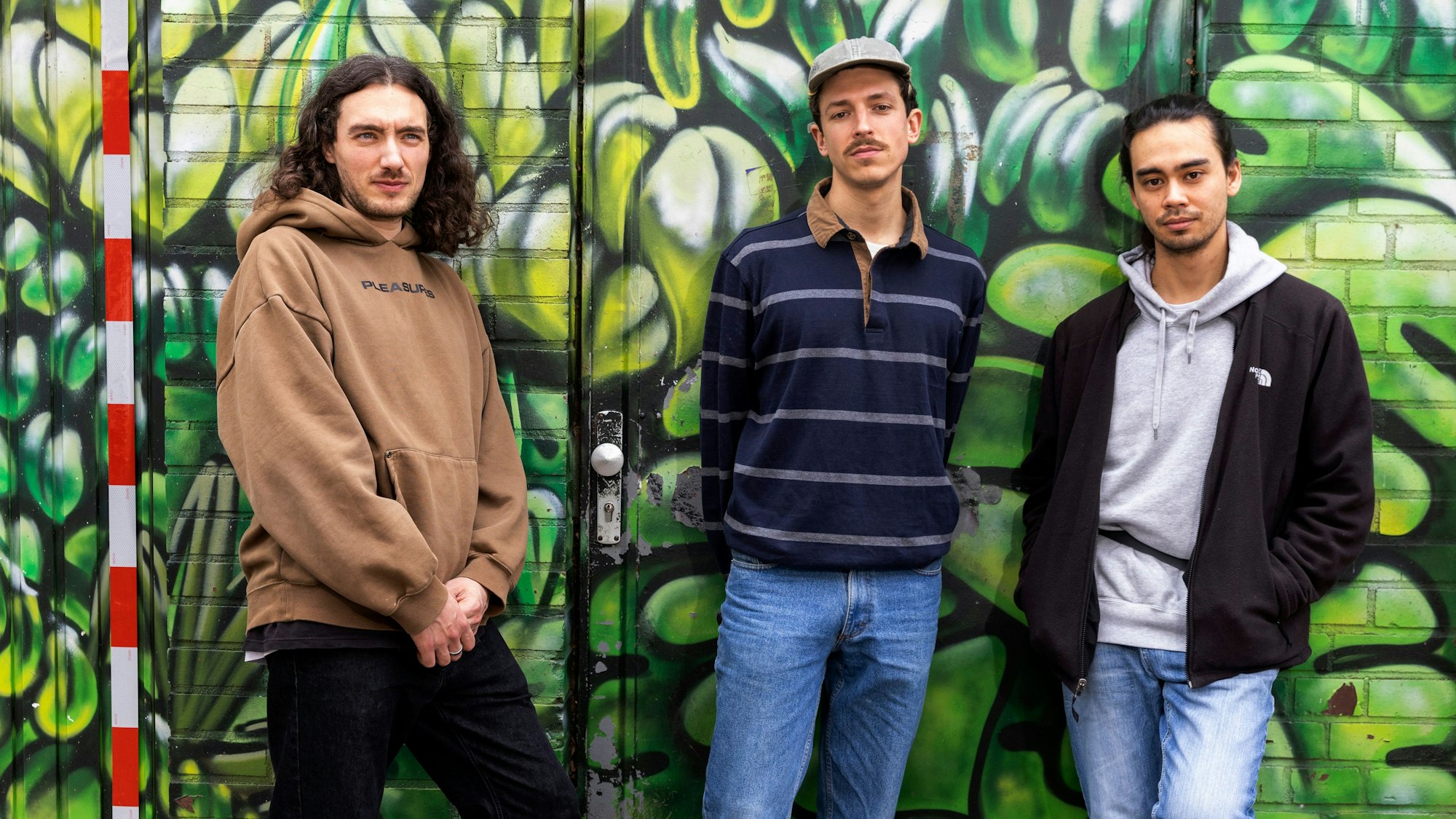 Philipp Schmid, Ben Werchohlad und Eric Wieben stehen vor einer grün besprayten Wand