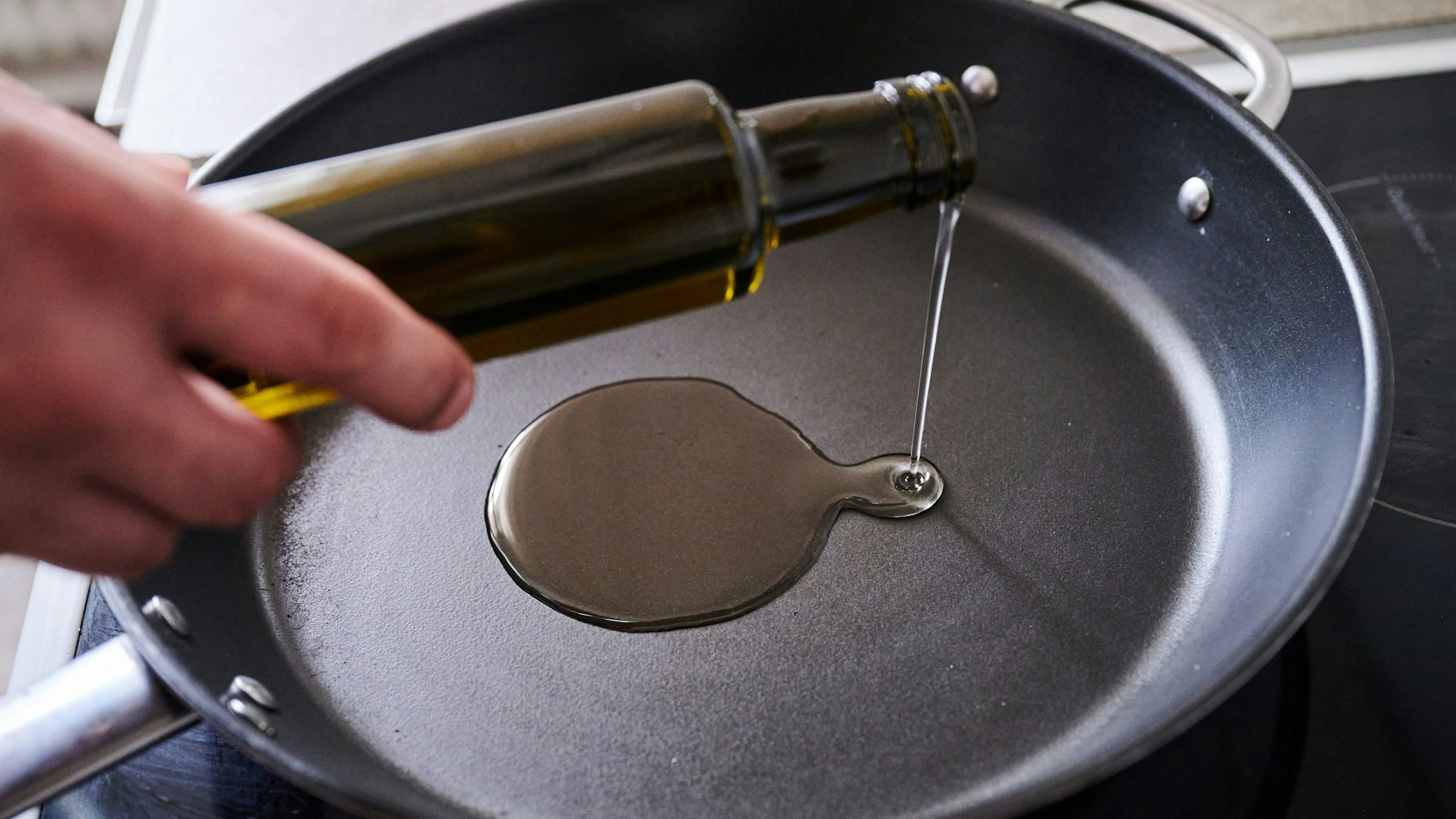 Jemand schüttet Sonnenblumenöl in eine Pfanne.