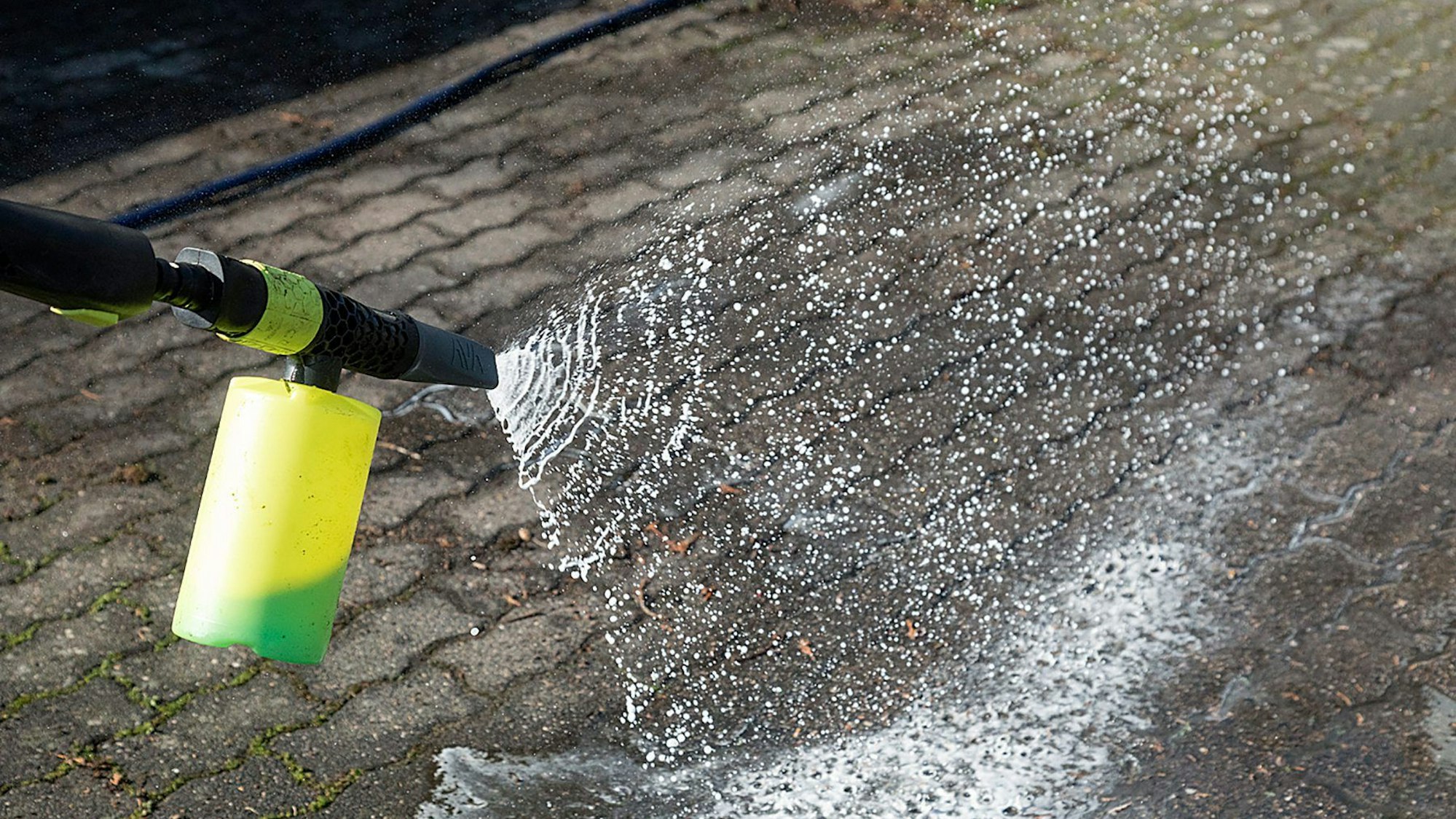 Ein Hochdruckreiniger sprüht Wasser mit Putzmittel auf Asphalt.