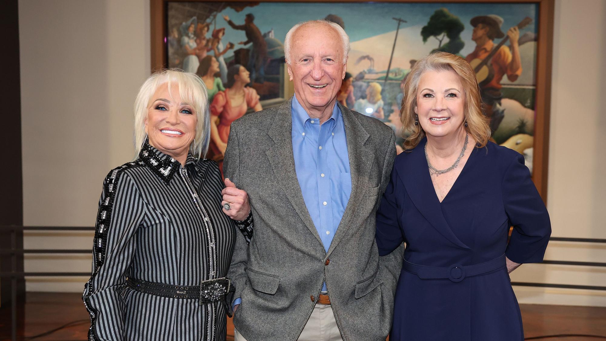 Tanya Tucker, Bob McDill und Patty Lovelesss posieren Arm in Arm bei einer Pressekonferenz.