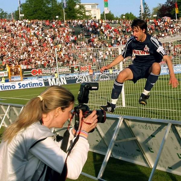 Ein Fußballer im dunkelblauen Trikot springt vor Freude über die Werbebande. Im Vordergrund ist eine Fotografin zu sehen.