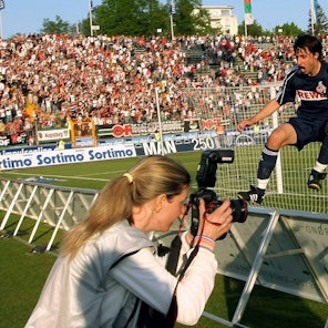 Ein Fußballer im dunkelblauen Trikot springt vor Freude über die Werbebande. Im Vordergrund ist eine Fotografin zu sehen.