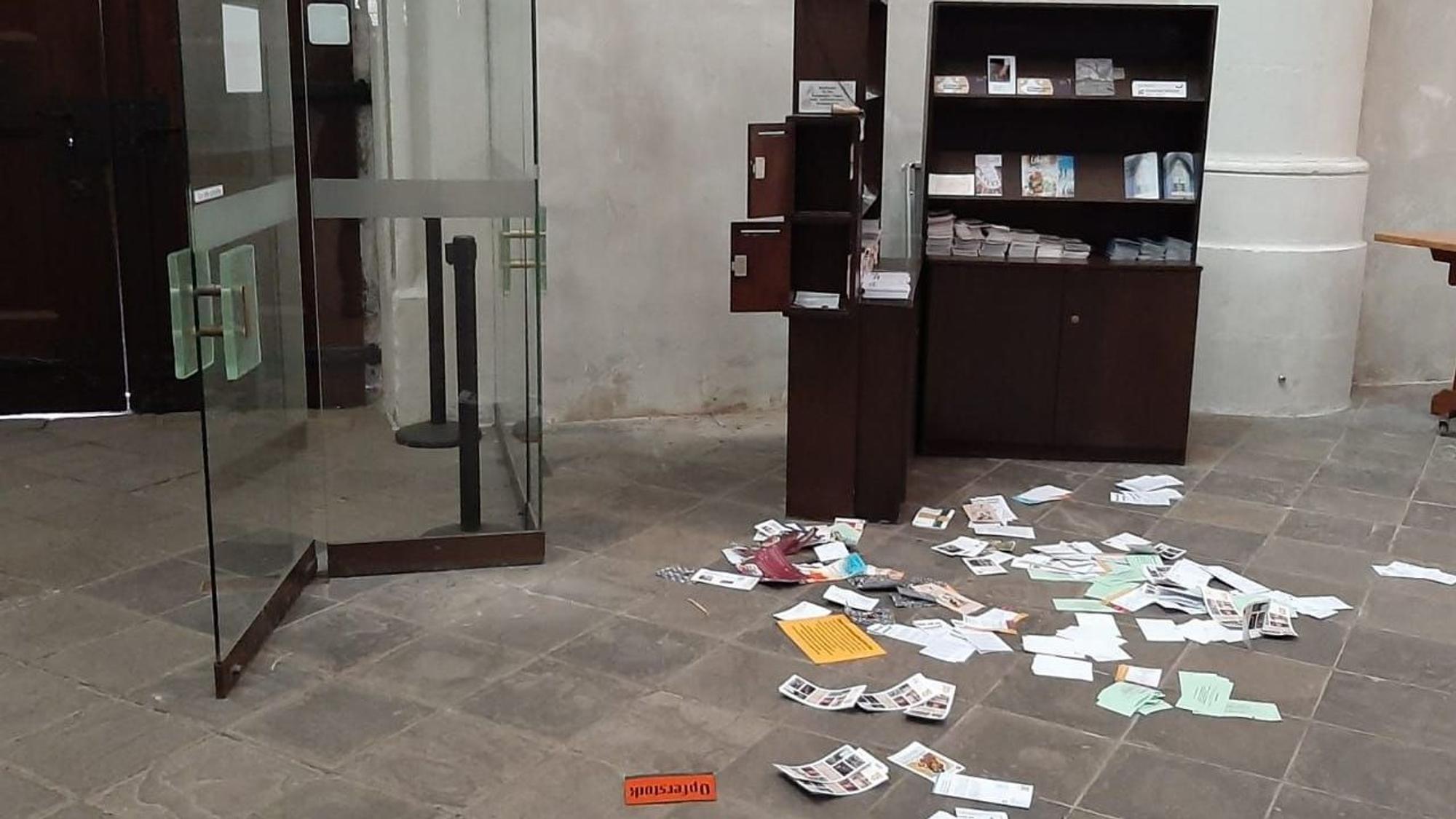 Broschüren und Schriften liegen auf dem Boden neben einer Kirchentür, der Schriftenstand ist aufgebrochen, Opferstöcke sind komplett gestohlen worden. Auf dem Boden liegt ein Schild mit der Aufschrift „Opferstock“.