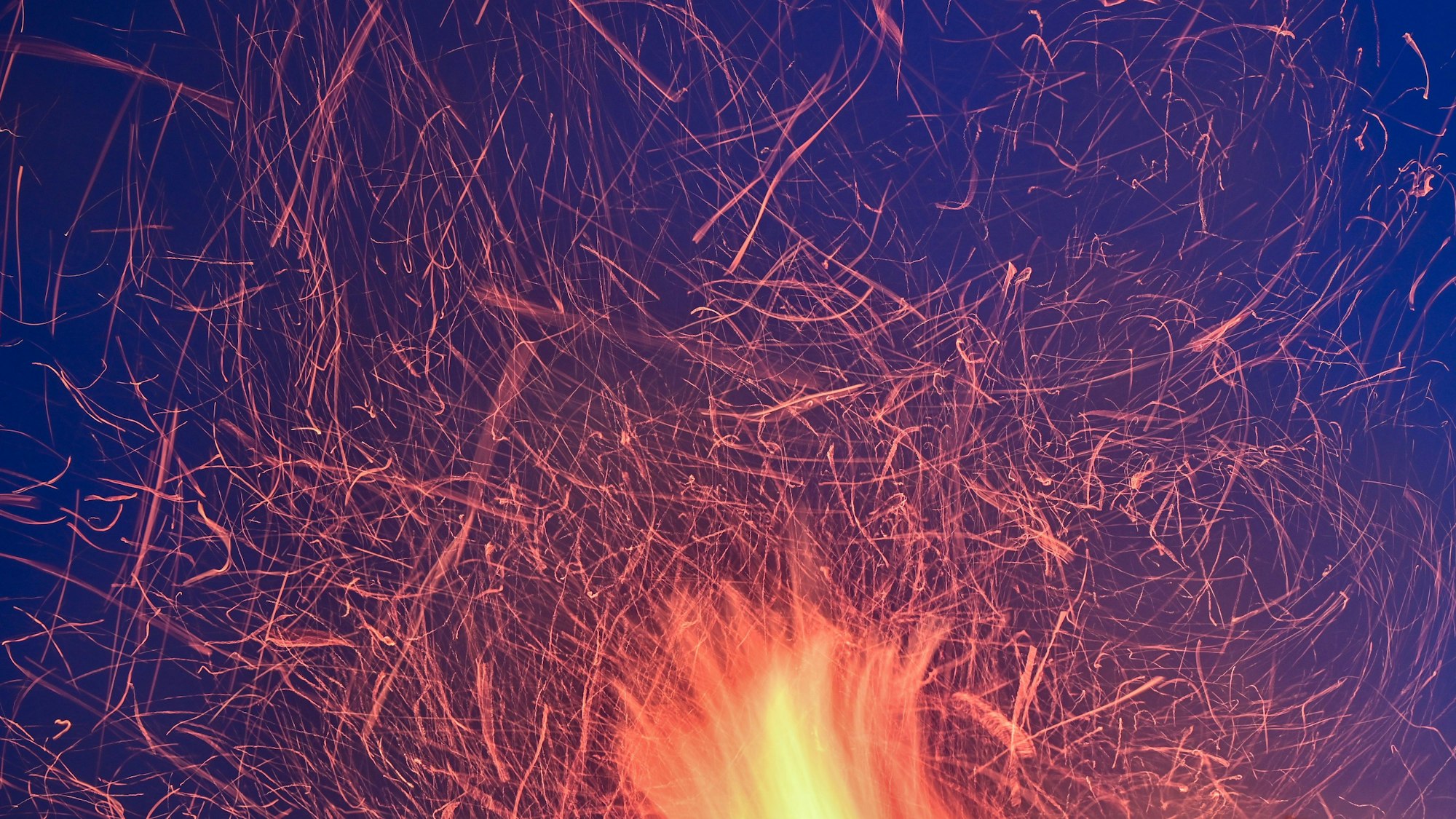 Funken eines Osterfeuers heben sich als Lichtspuren vor dem blauen Abendhimmel ab.