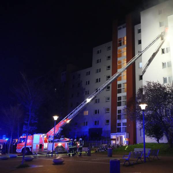 Feuerwehrfahrzeug mit Kran vor einem brennenden Hochhaus