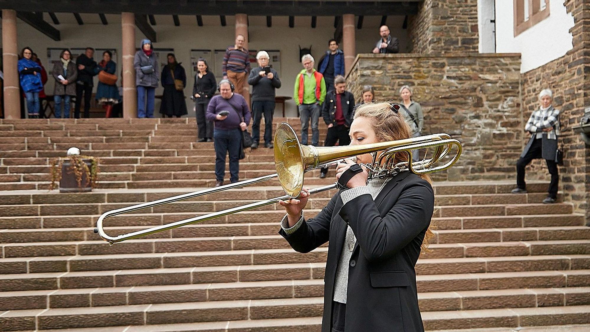 Im Vordergrund ist die Musikerin mit ihrer Bassposaune zu sehen, auf den Stufen dahinter lauschen die Besucher.