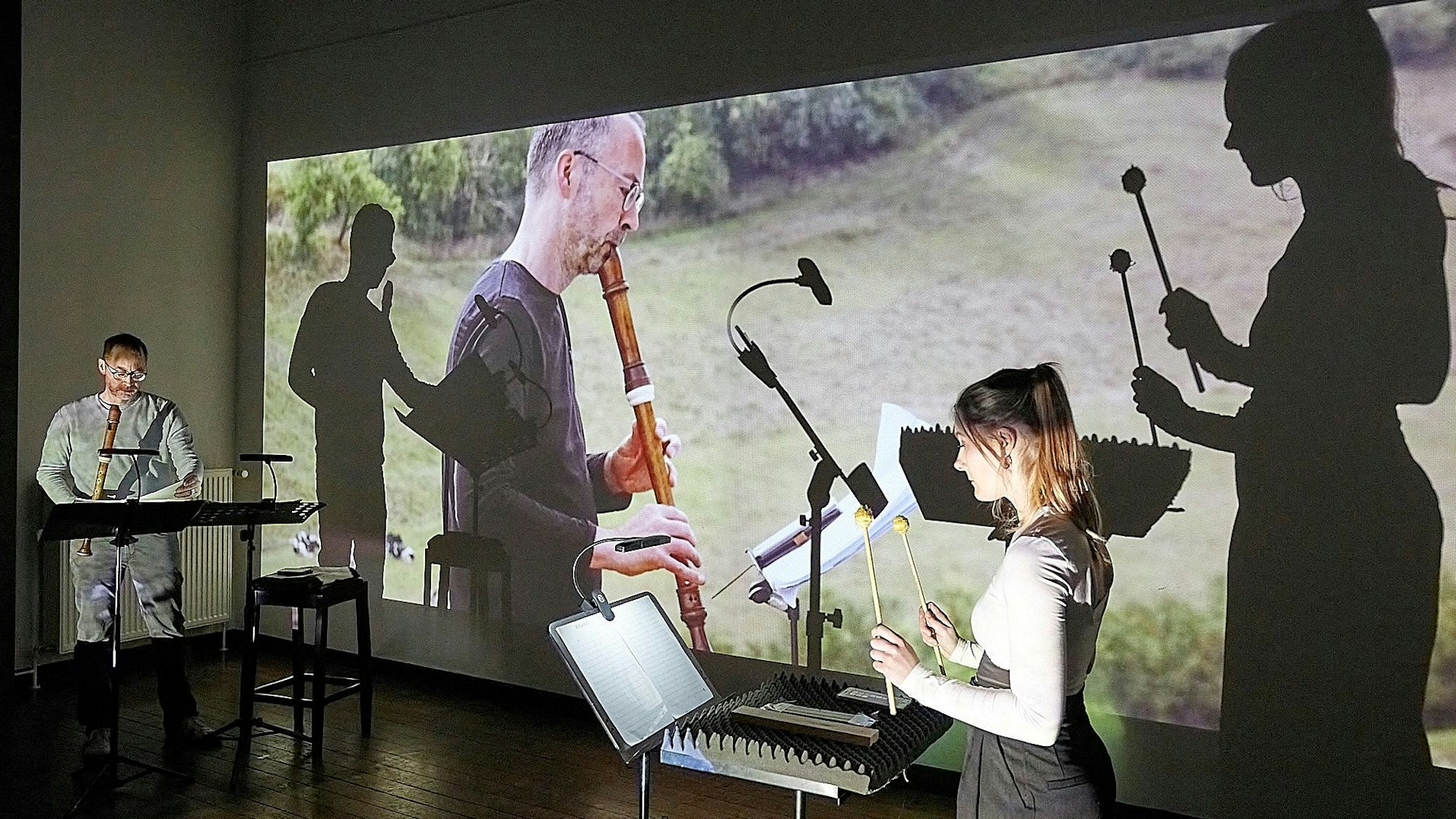 Die beiden Musiker spielen vor einer Videoleinwand. Dort mischen sich ihre Schatten mit dem Film, der sie bei Musikaufnahmen mit dem gleichen Stück auf dem Kalvarienberg bei Alendorf zeigt.