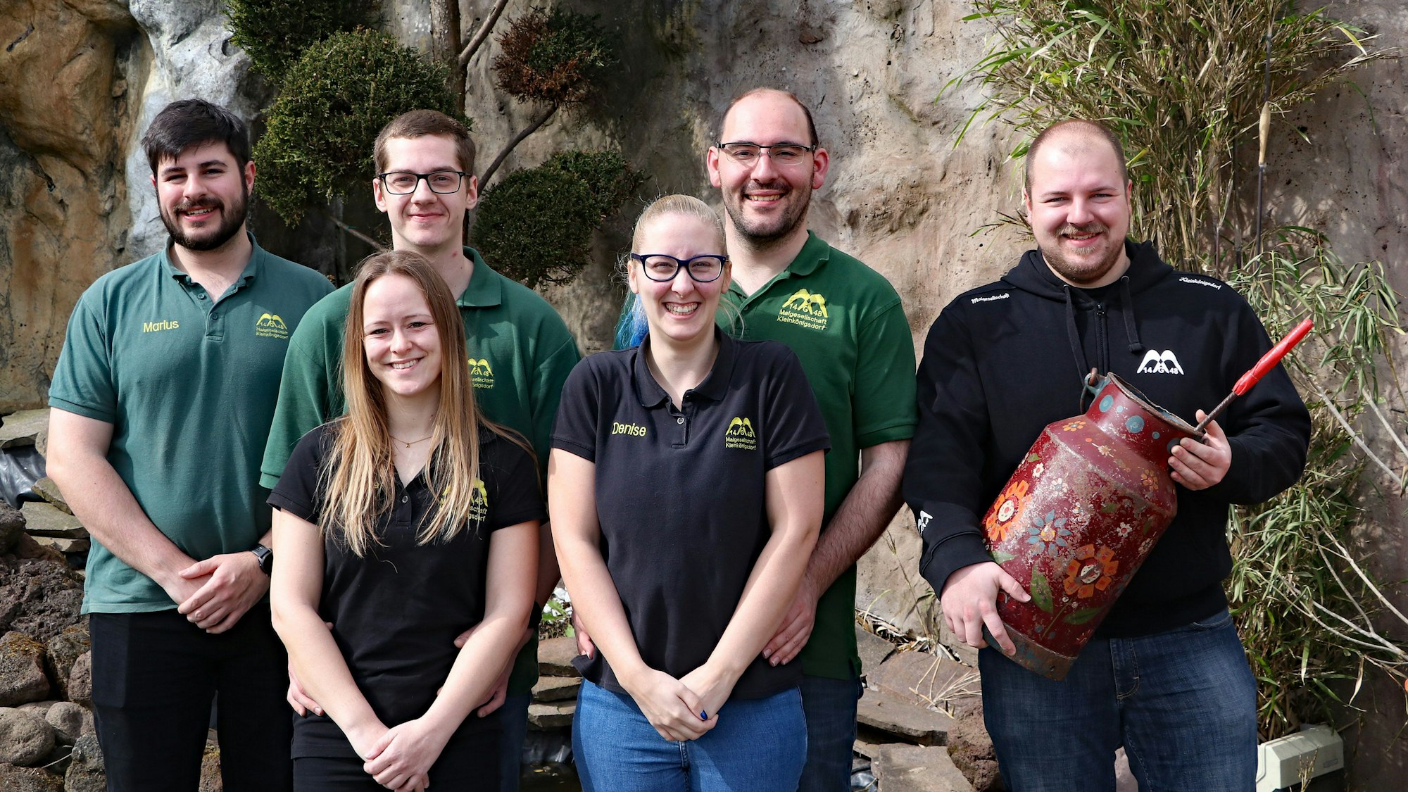 Es sind die im Text genannten Titelträger zu sehen. Sie stehen in zwei Reihen nebeneinander und lächeln in die Kamera.