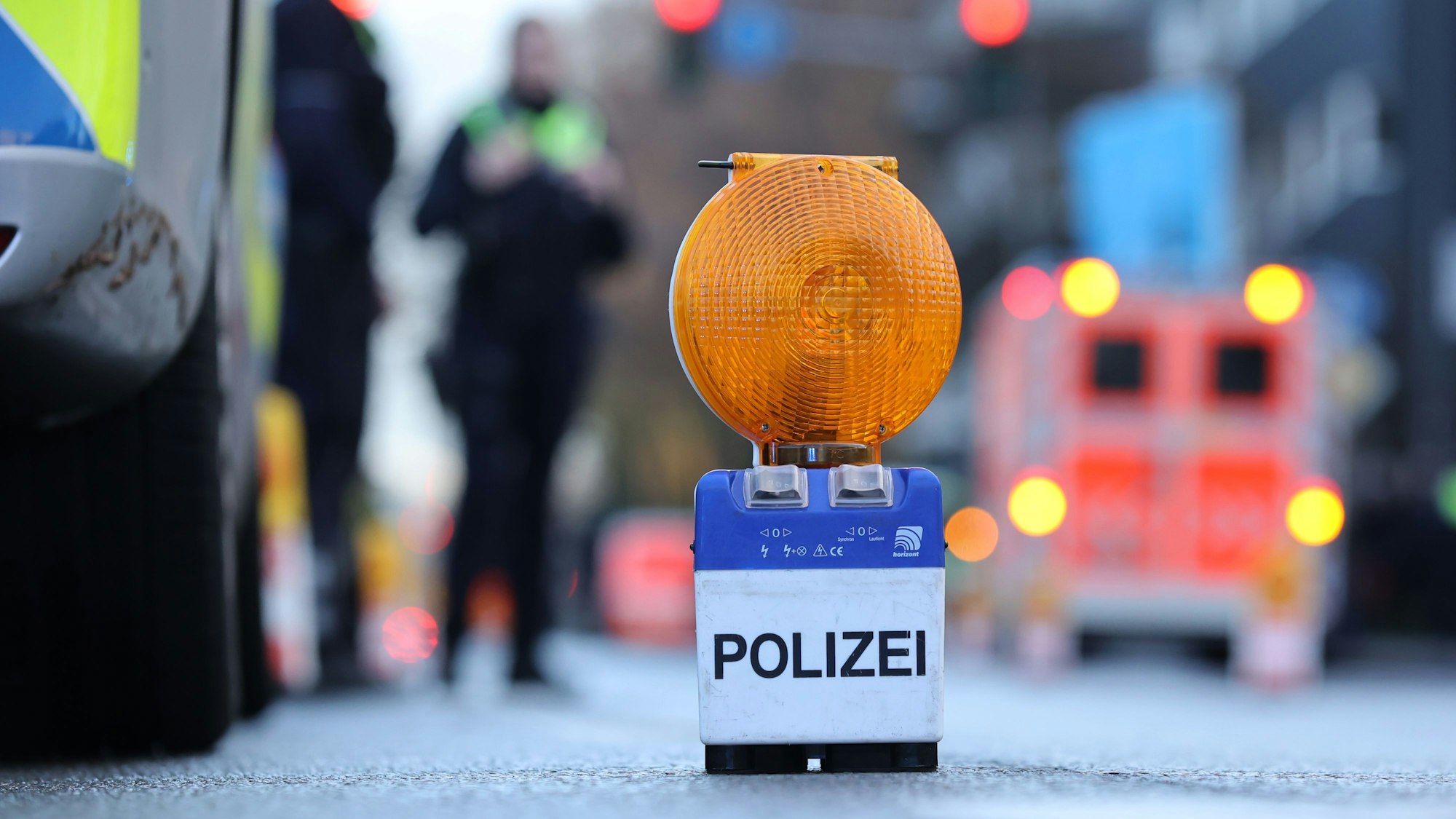Polizei-Warnbake auf Aachener Str. mit Rettungswagen und Beamten im Hintergrund.