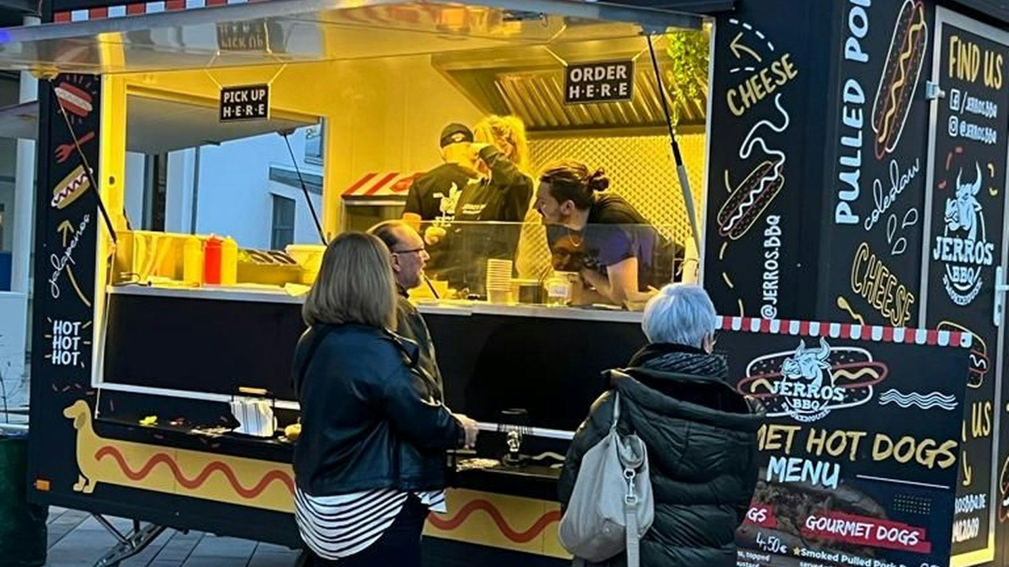 Es ist ein Streetfood-Wagen zu sehen, vor dem mehrere Leute stehen.