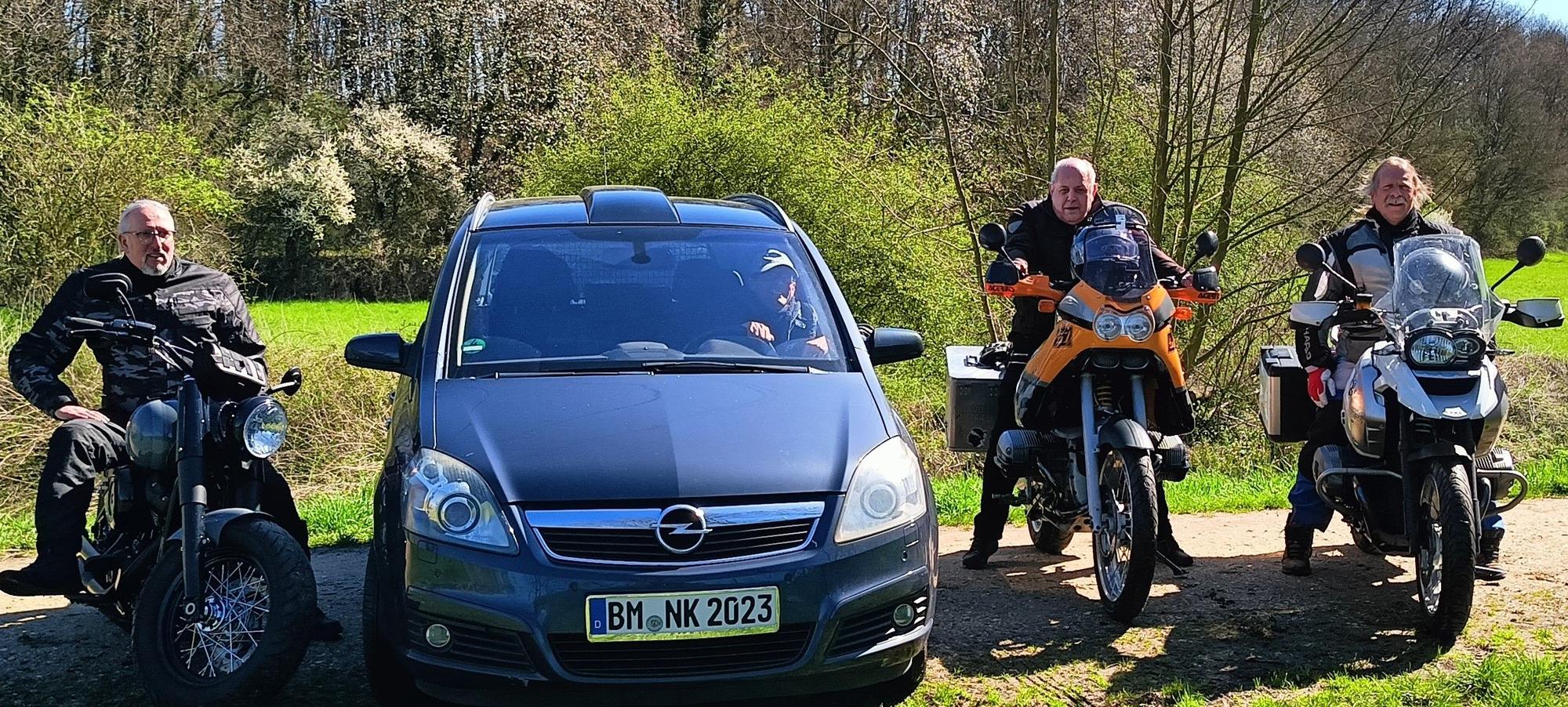 Die Abenteurer sitzen vor ihrer Reise zum Nordkap auf Motorrädern. Einer von ihnen sitzt in einem Auto.