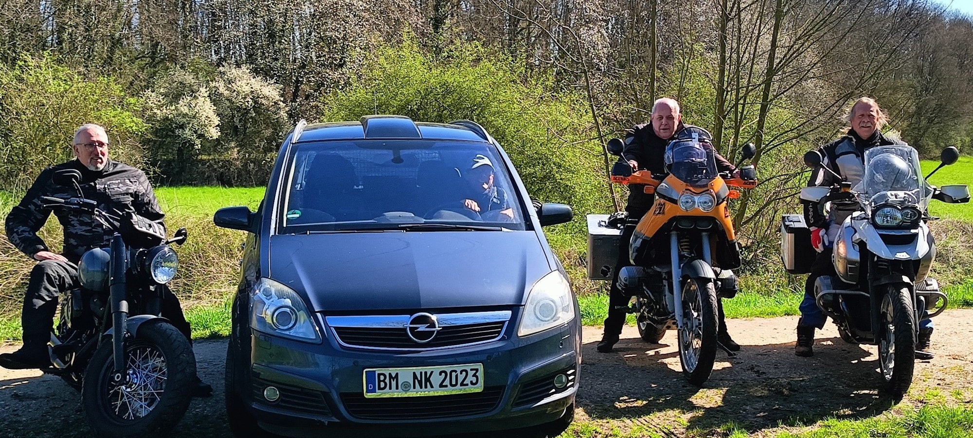 Die Abenteurer sitzen vor ihrer Reise zum Nordkap auf Motorrädern. Einer von ihnen sitzt in einem Auto.