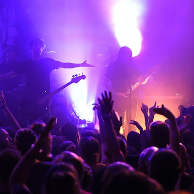 Eine Menschenmenge vor einer Bühne, darauf Gitarristen.