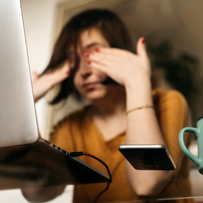 Junge Frau reibt sich die Augen vor ihrem Laptop