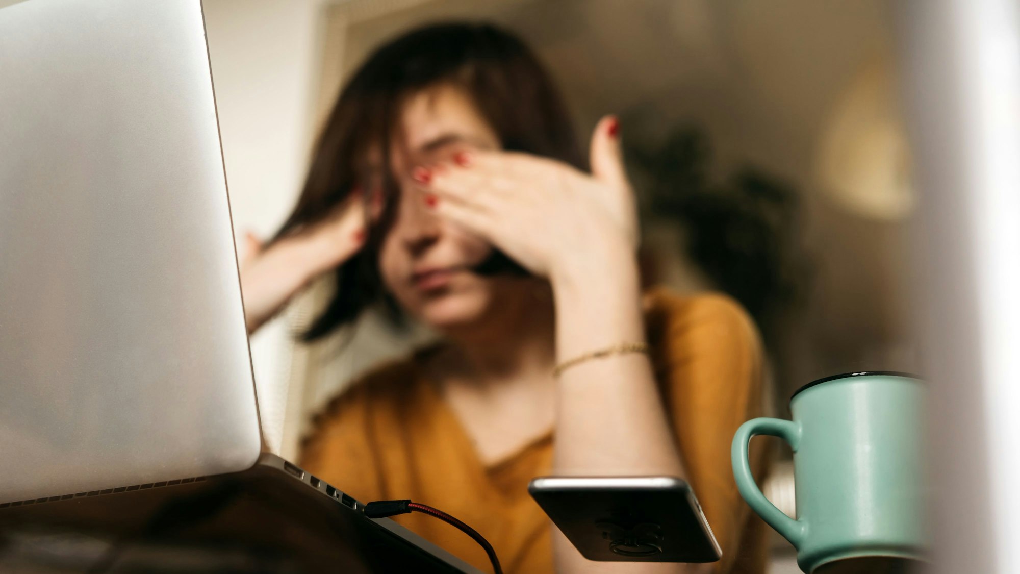 Junge Frau reibt sich die Augen vor ihrem Laptop