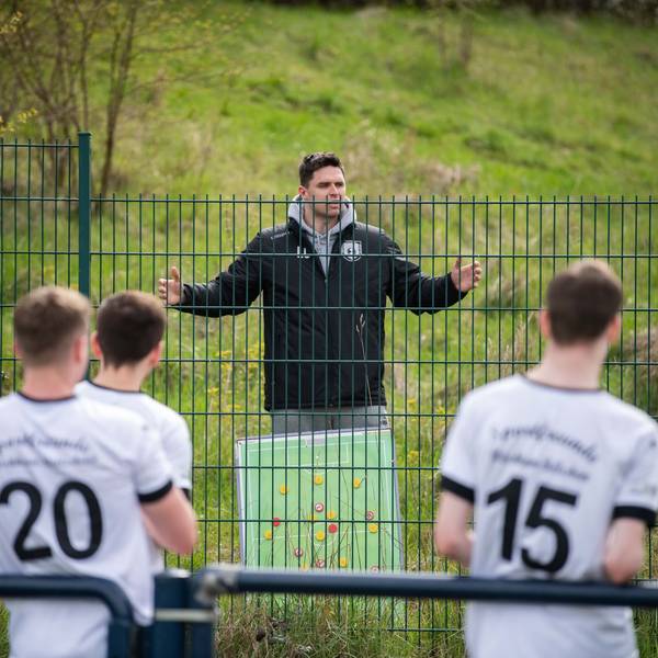 Hinter Gittern: Trainer Lucas Carell hält Abstand und gibt in der Halbzeit taktische Anweisung hinter dem grünen Zaun, der um den Kunstrasenplatz gezogen worden ist.