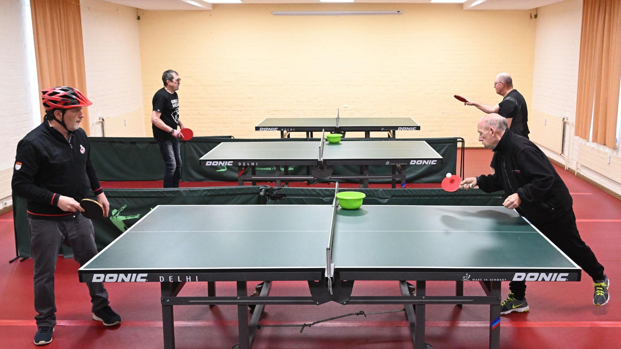 Vier Menschen spielen an zwei Tischtennisplatten Tischtennis.