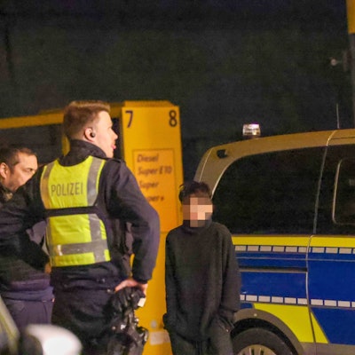 Ein Kind, das Gesicht ist verpixelt, steht neben einem Polizisten und einem Polizeiwagen.