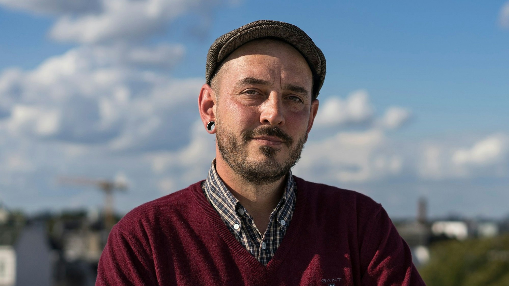 Ein Mann mit einer Baskenmütze und Tunnelohrringen im Porträt.