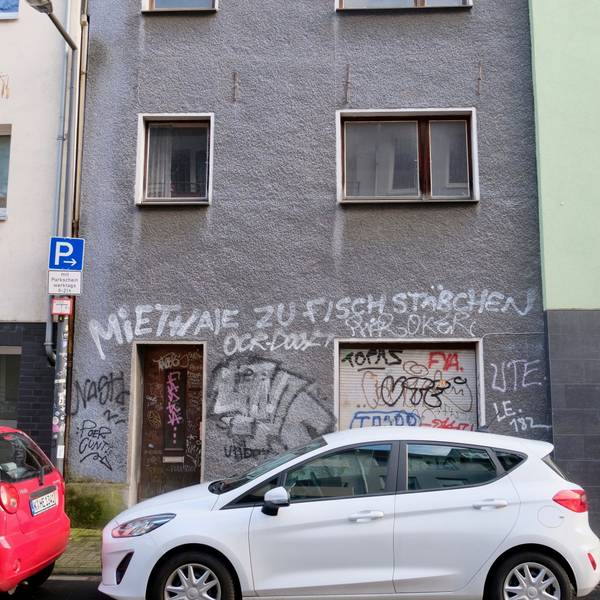 Ein runtergekommenes, unbewohntes Haus in der Kölner Glasstraße 6, mit grauer Fassade, auf die der Spruch „Miethaie zu Fischstäbchen“ gesprüht ist, steht seit mindestens 15 Jahren leer.