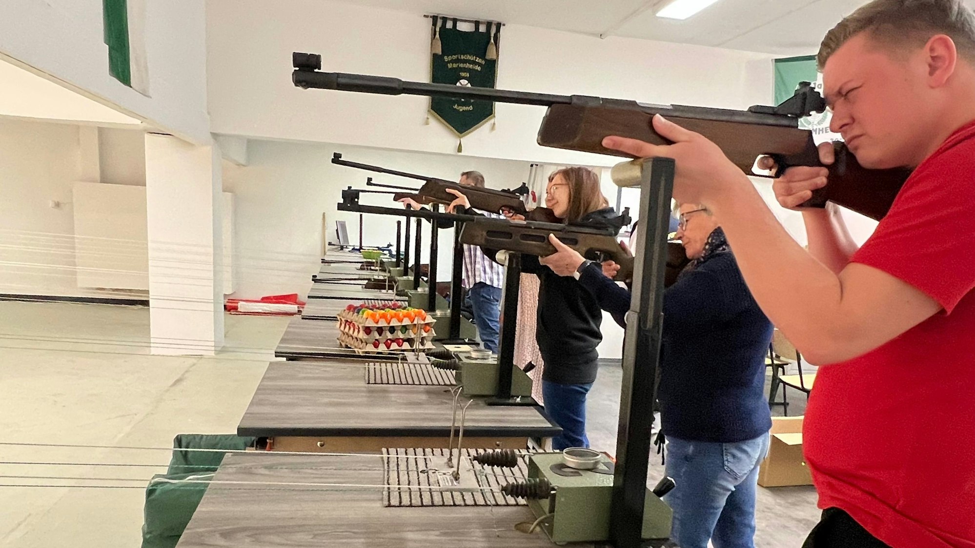 Am Schießstand stehen mehrere Schützinnen und Schützen mit dem Gewehr im Anschlag.