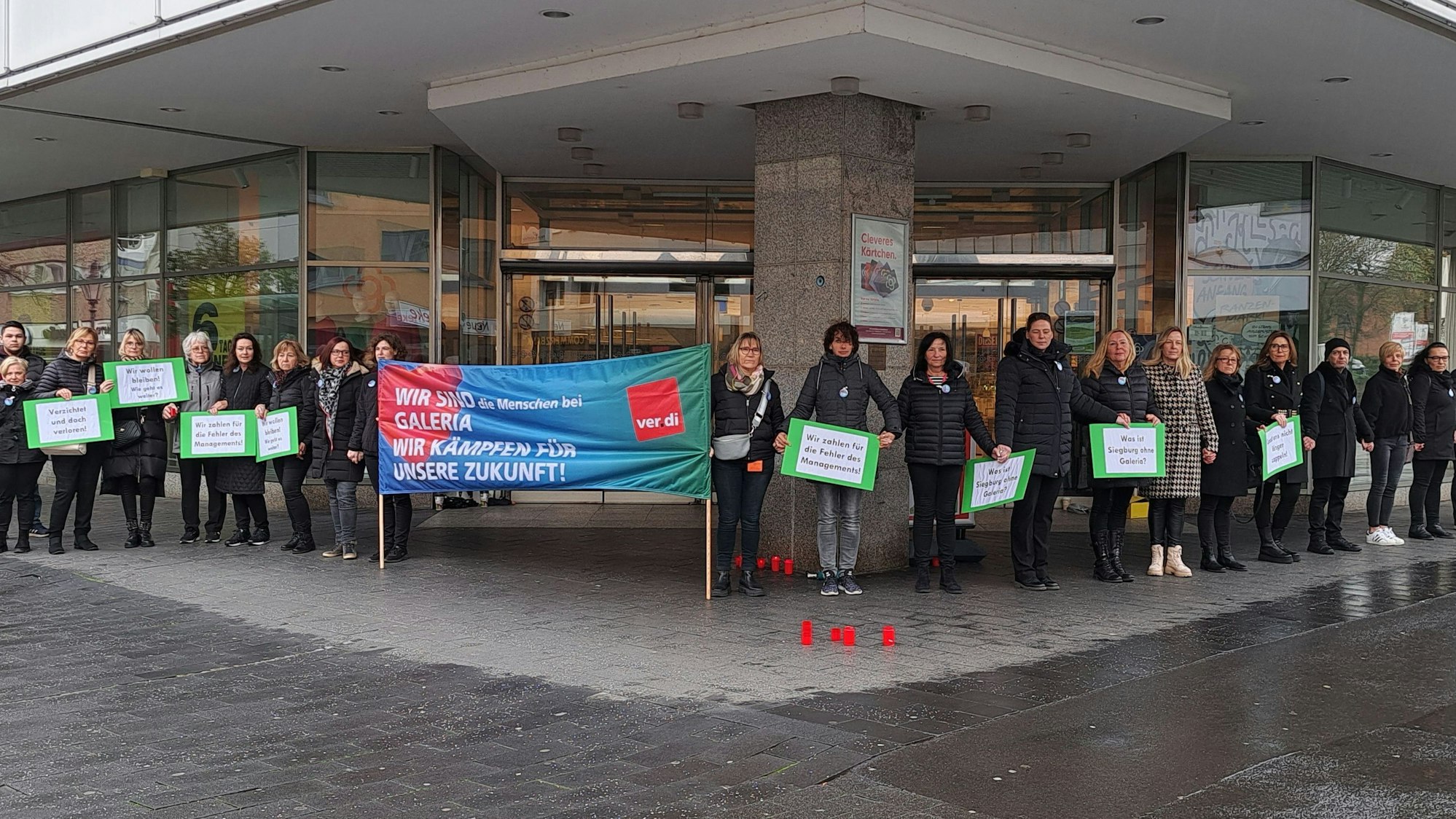 Beschäftigte der Siegburger Filiale von Galeria Karstadt Kaufhof stehen mit Schildern und Bannern vor der Filiale.