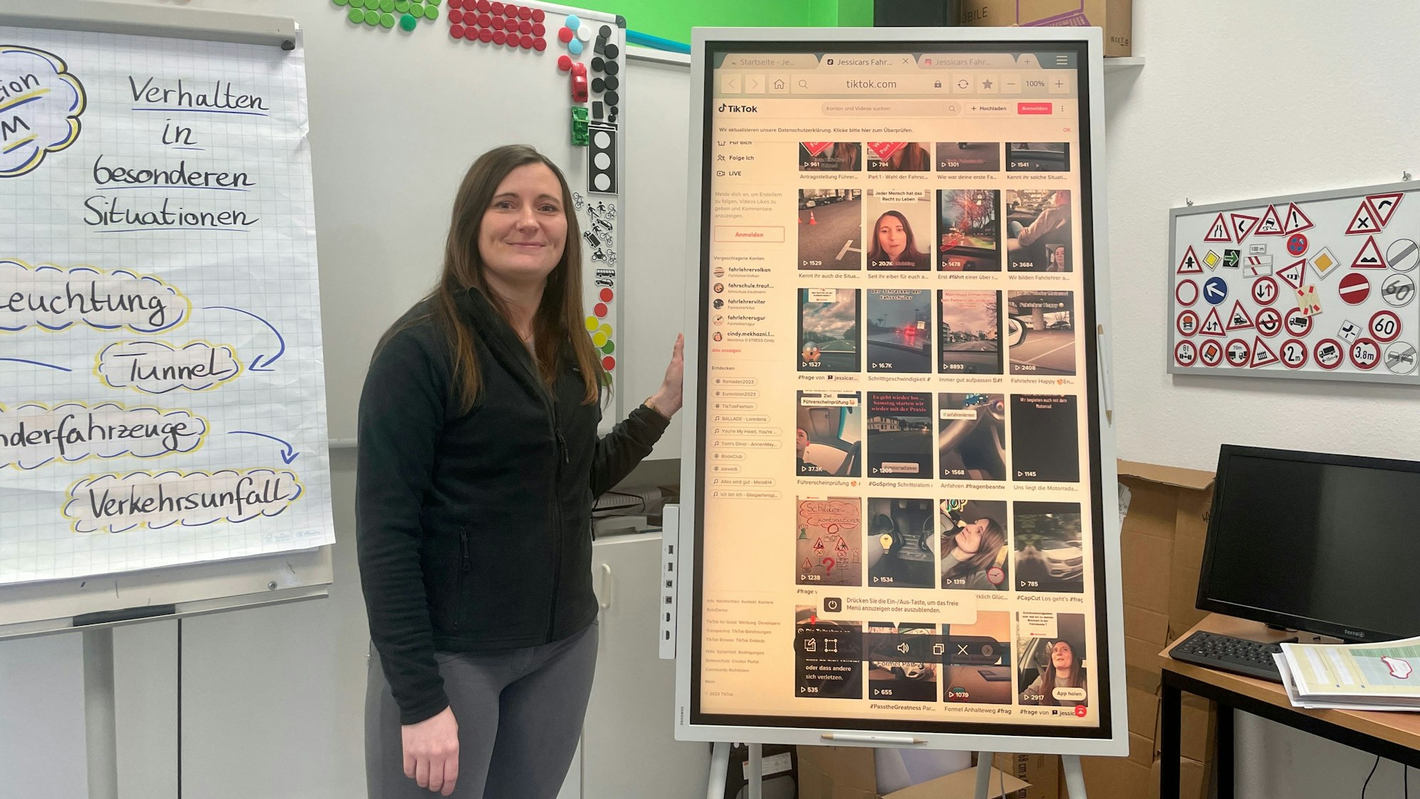 Jessica Richartz vor einem digitalen Whiteboard, auf dem ihre Tiktok-Seite angezeigt wird, in ihrer Leverkusener Fahrschule „Jessicars Fahrschule“.