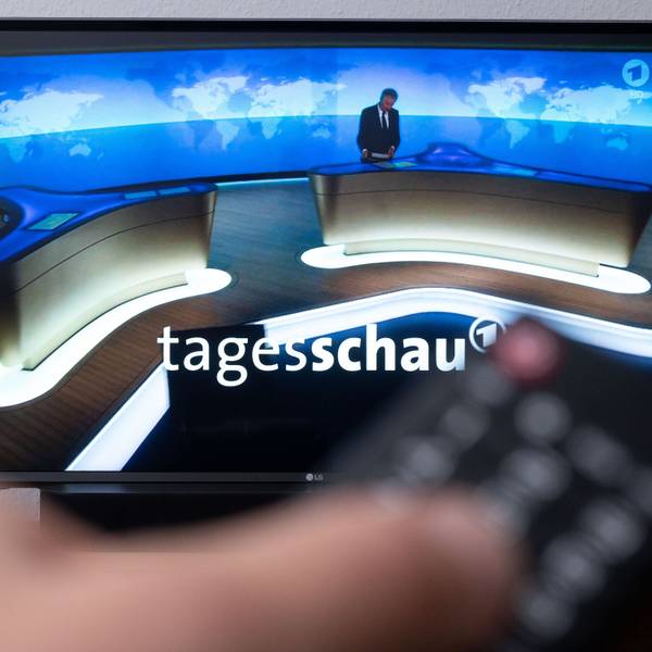 Ein Mann hält eine Fernbedienung vor einen Fernseher, auf dem die Tagesschau läuft.