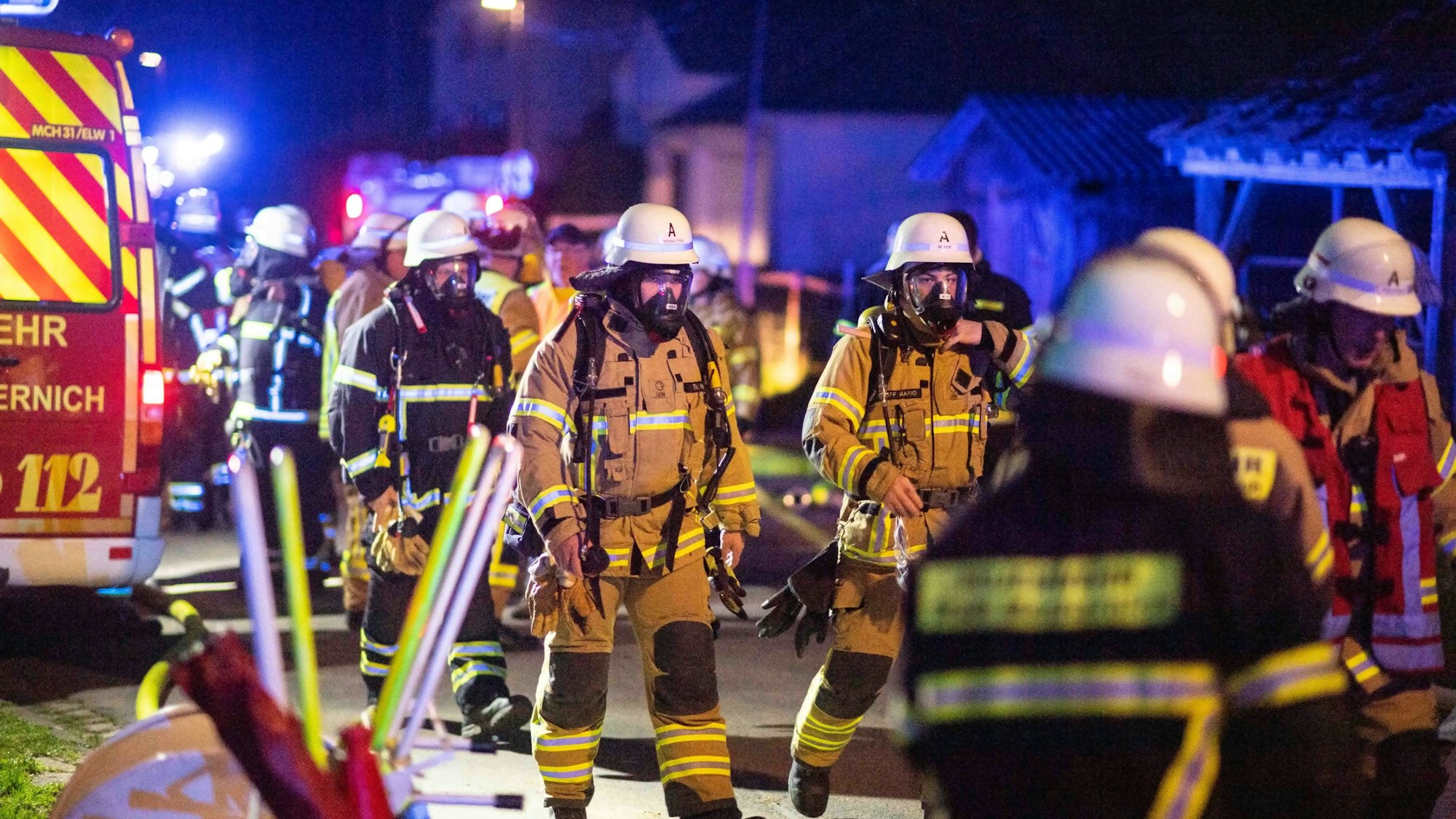 Feuerwehrleute mit Atemschutz gehen zum Brandort. Viele andere Feuerwehrleute arbeiten drumherum.