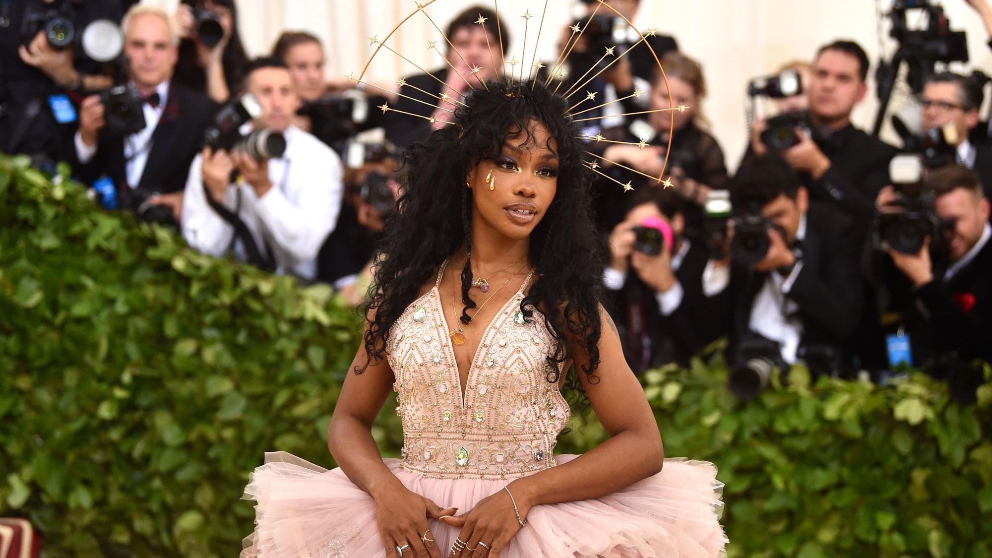 SZA steht in einem Perlenkleid und einer Krone auf dem roten Teppich.