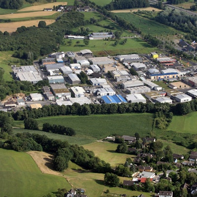 Aus der Vogelsperspektive ist ein Gewerbegebiet inmitten von Feldern zu erkennen und daneben, von einer Straße getrennt, die Anlage der Burg Sülz.
