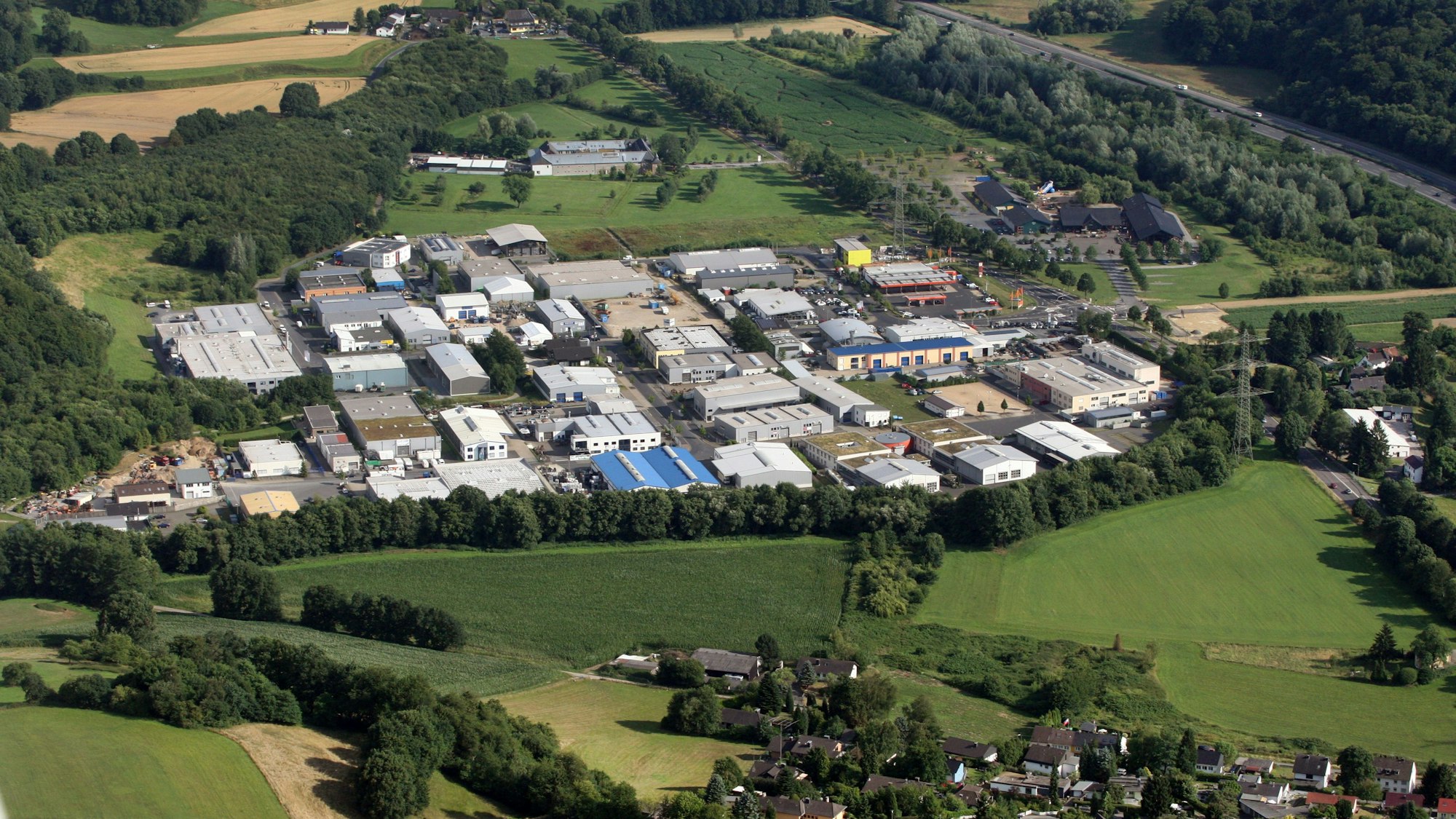 Aus der Vogelsperspektive ist ein Gewerbegebiet inmitten von Feldern zu erkennen und daneben, von einer Straße getrennt, die Anlage der Burg Sülz.