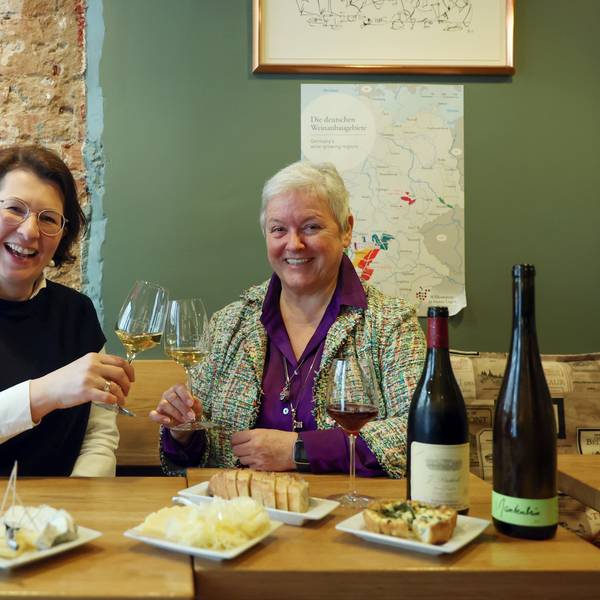 Zwei Frauen sitzen an einem gedeckten Tisch und prosten sich mit Weißwein zu