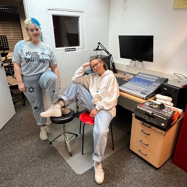 Zwei junge Frauen, sportlich gekleidet, sitzen lässig und mit jeweils einem Fuß auf einen Stuhl gestellt, in einem Tonstudio.