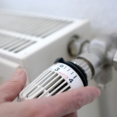 Eine Frau dreht an einem Heizungsthermostat.