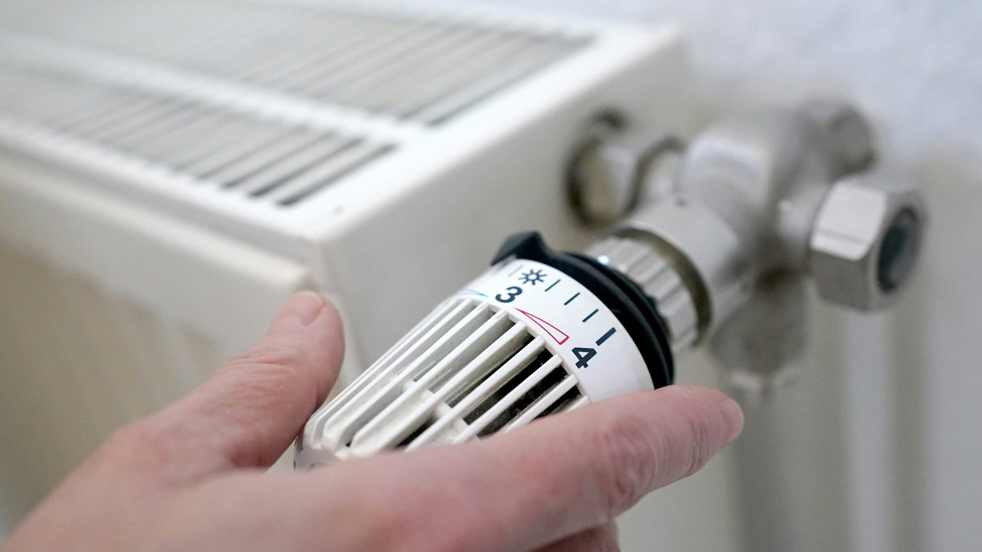 Nahaufnahme einer Heizung. Eine Frau dreht an einem Heizungsthermostat.