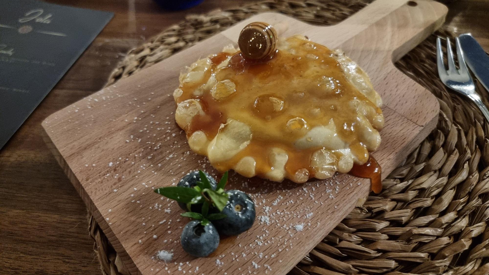 frittierte Teigtasche auf einem Holzbrett, darüber Honig