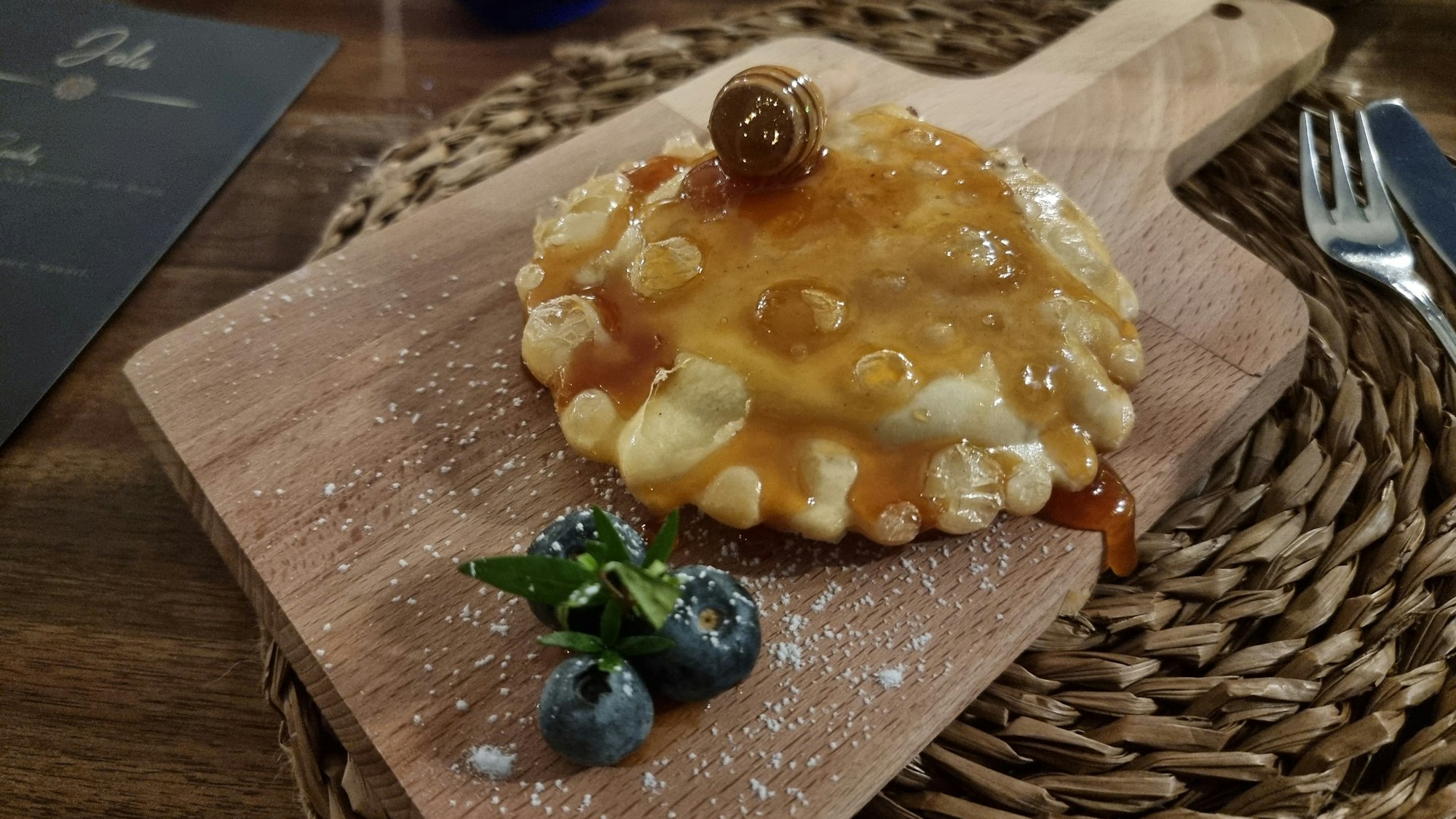frittierte Teigtasche auf einem Holzbrett, darüber Honig