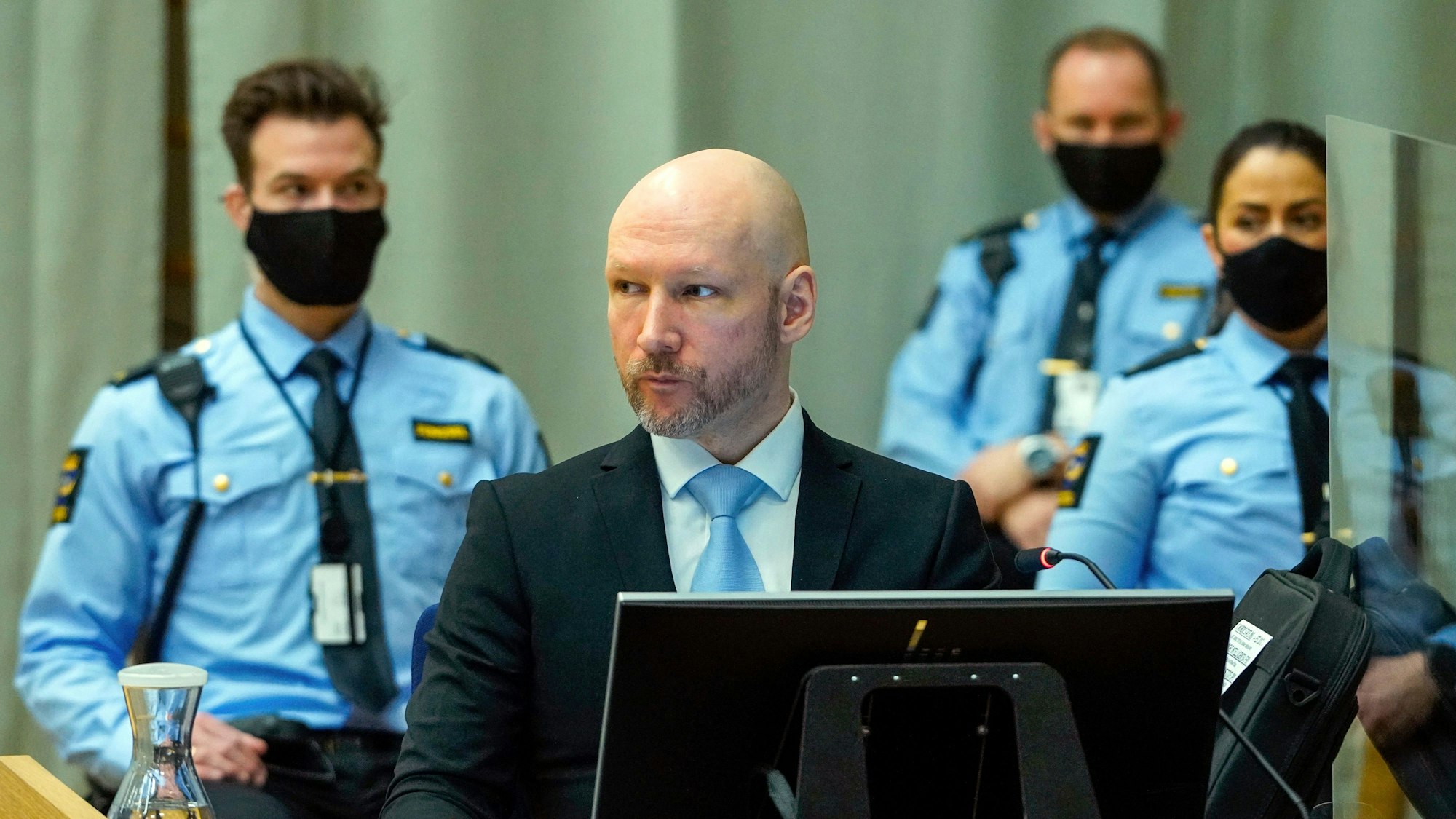Anders Behring Breivik sitzt bewacht im Gefängnis.Er trägt einen dunklen Anzug und eine hellblaue Krawatte.