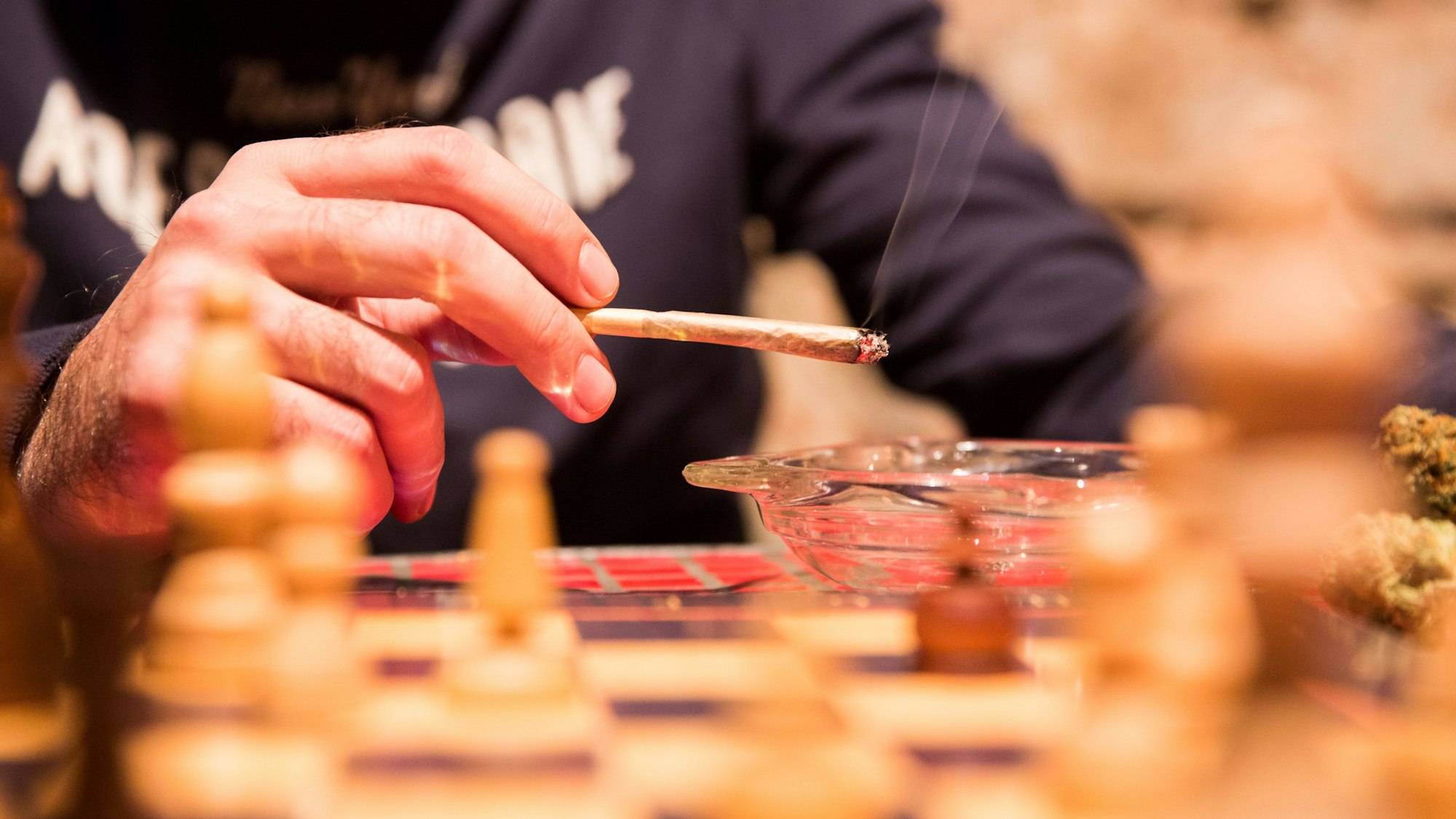 Ein Mann sitzt in einem spanischen Cannabis Social Club und raucht einen Joint. Neben dem erhältlichen Cannabis gibt es auch Freizeitaktivitäten wie Schachspiele oder Fernseher.