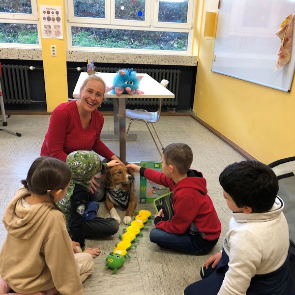 Sonja Mies sitzt auf der Erde. An ihrer Seite liegt Casper. Drei Jungs und ein Mädchen sitzen in einem Halbkreis mit ihr.