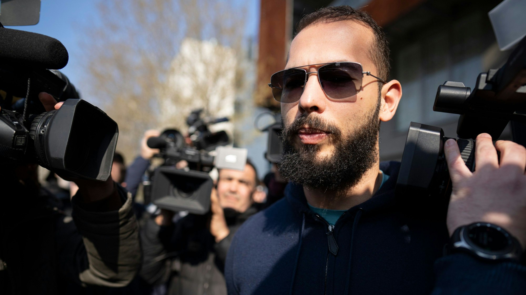 Der frauenfeindliche Andrew Tate mit Sonnenbrille ist von Kameras umringt