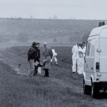 Das historische Foto zeigt einen Transporter der Polizei, der auf einem Feldweg steht. Um ihn herum stehen Menschen.