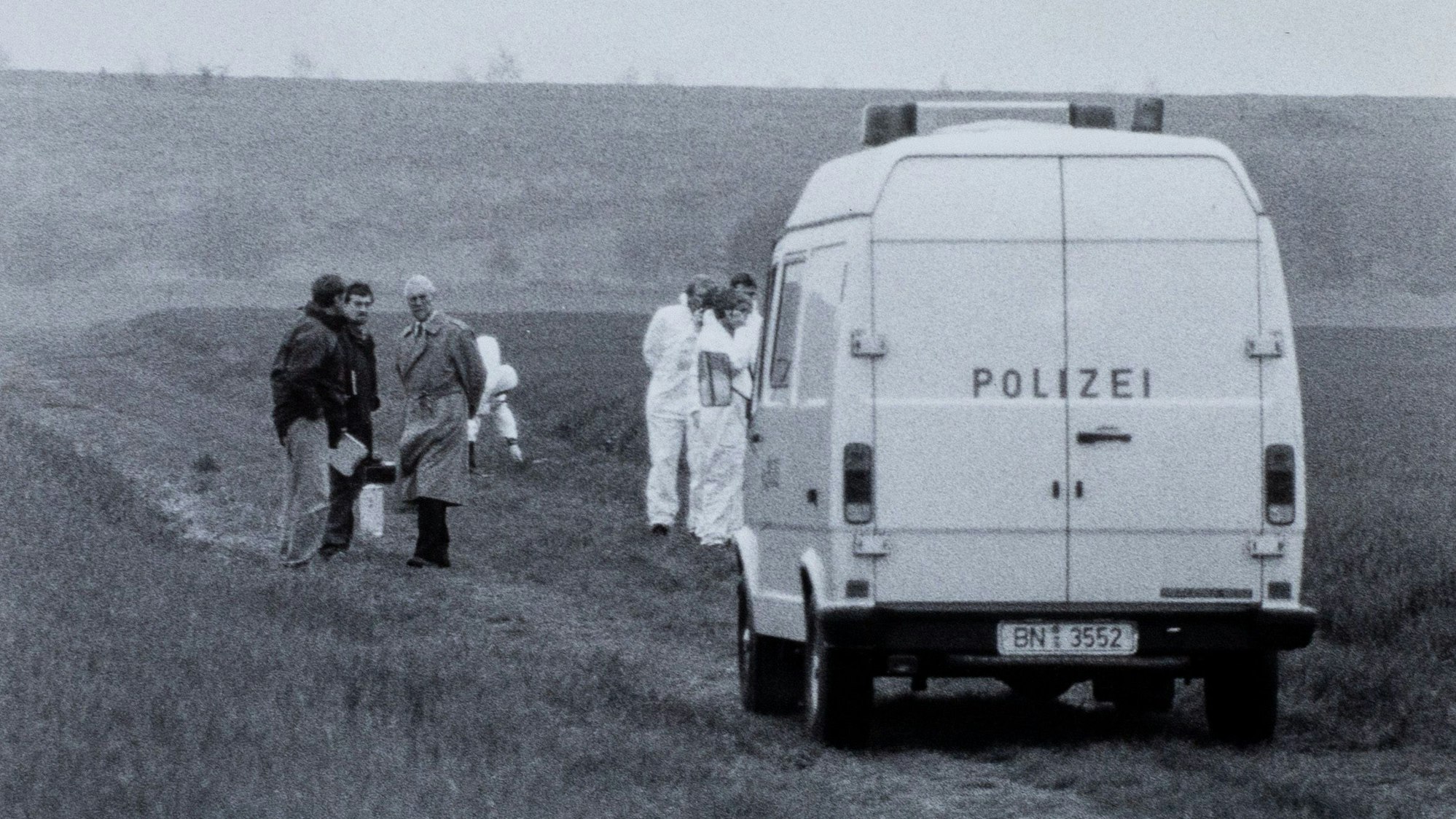 Das historische Foto zeigt einen Transporter der Polizei, der auf einem Feldweg steht. Um ihn herum stehen Menschen.