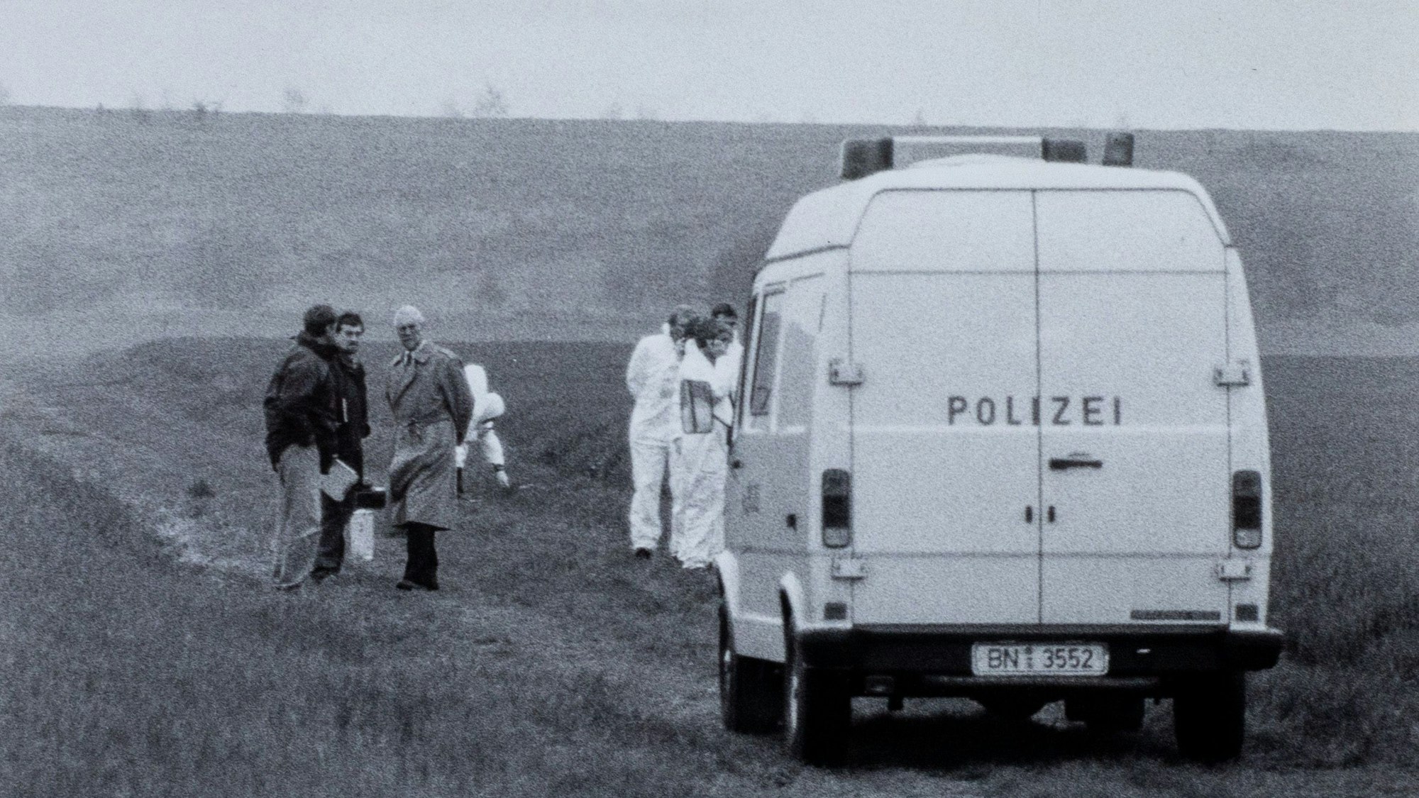 Ein Polizeiauto steht auf einem Feldweg. Das Bild ist in schwarz-weiß.