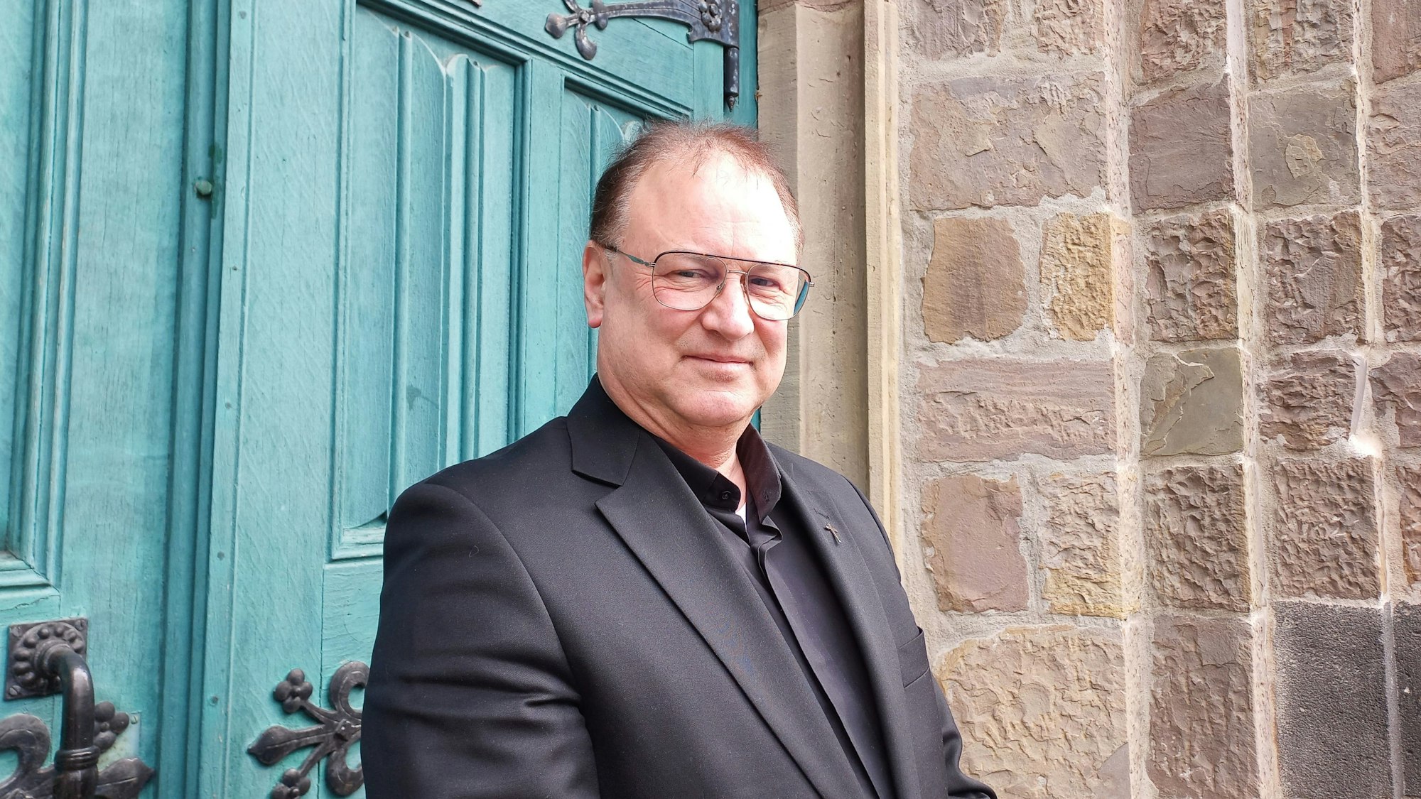 Michael Enders trägt einen schwarzen Anzug, ein schwarzes Hemd und lächelt in die Kamera.