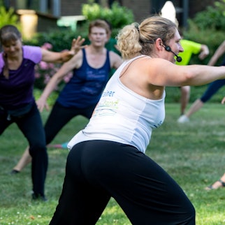 Das Bild zeigt eine Gruppe mit Fitnesstrainerin bei Sport im Park.