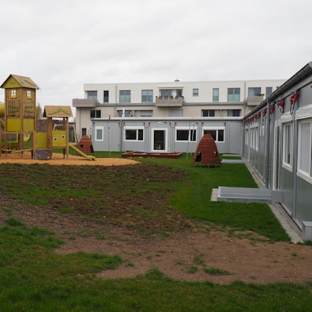 Zu sehen sind links ein riesiges Spielgerüst und rechts das Kita-Gebäude.