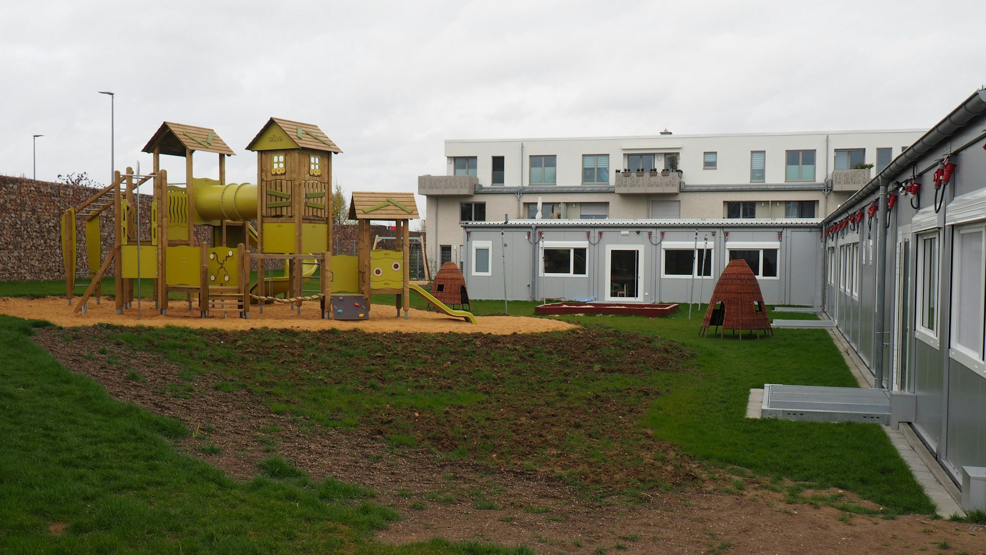 Zu sehen sind links ein riesiges Spielgerüst und rechts das Kita-Gebäude.