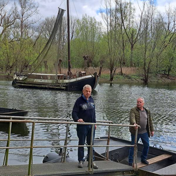 Die zwei Männer stehen am Wasser. Im Hintergrund ist das Schiff zu sehen.